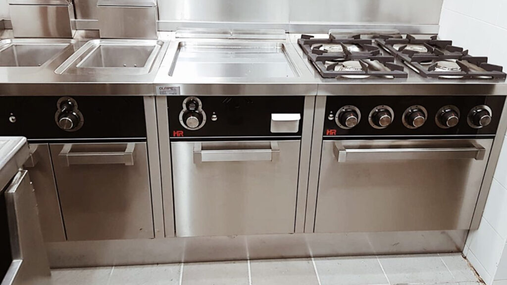 Línea de cocción industrial de acero inoxidable con plancha, fuegos de gas y hornos para cocina profesional.