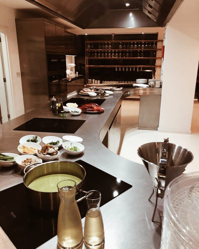 Cocina profesional de acero inoxidable con encimera en isla, placas de inducción y cuencos con ingredientes preparados.